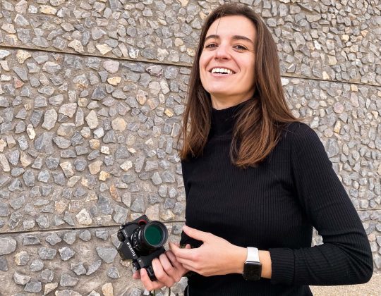 Me, a white girl with brown long hair wearing a turtleneck black t-shirt, holding a camera